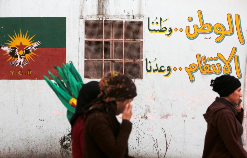 People walk next to a wall writing in the Sheikh Maksoud neighbourhood of Aleppo